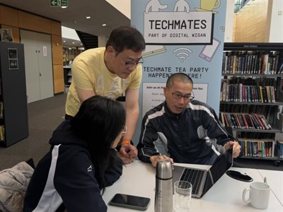 Three people sat around a laptop looking at the screen. One of them is standing up. A banner behind them says Techmates on it