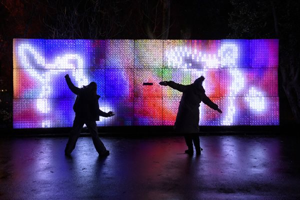 Shadows of two people dancing in front of a light installation