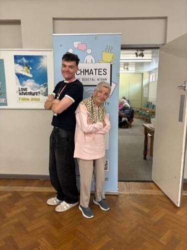 A young man and an older lady stood back to back with their arms folder in front of a banner that says techmates on it