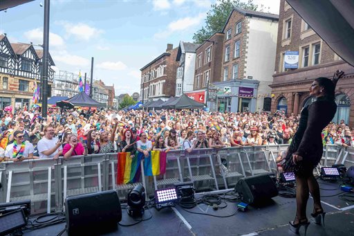 Musician on a stage in front of a large crowd with rainbow flags