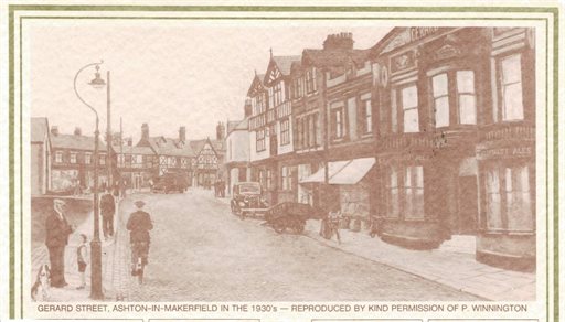 Artist impression of Gerard Street in the 1930s. The street is lined with shops and tall brick and timber‑framed buildings. A cyclist rides toward the camera, and a few pedestrians stand along the pavement. A vintage car is parked on the right, and an ol