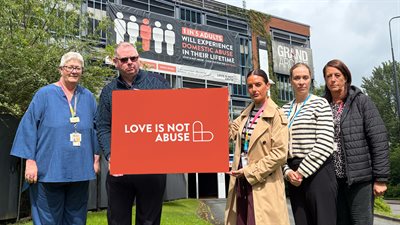 Wigan Borough community safety partnership members and domestic abuse service members holding the Love Is Not Abuse poster in Wigan
