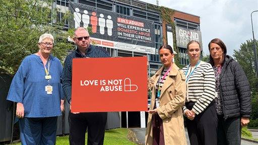 Wigan Borough community safety partnership members and domestic abuse service members holding the Love Is Not Abuse poster in Wigan