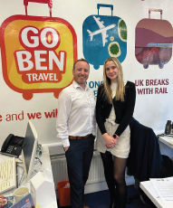 Two people stood by a sign with three suitcases, one of them saying Go Ben Travel