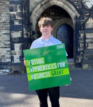 A young man standing in front of an arcway holding a FAB grant sign