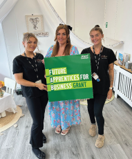 Three ladies stood holding a green sign saying future apprentices for business grant