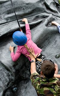 Child rockclimbing being helped by armed forces personnel