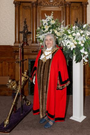 Mayor dressed in red robe with white flowers on a stand next to her