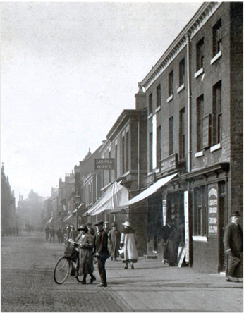 Old street with people walking around. A lady is pushing a bike in the road.