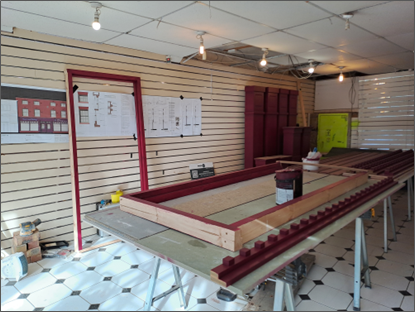 Inside bradshawgate where a long red wooden frame and matching panels sit on tables, with tools and a paint bucket