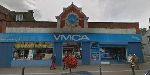 Exterior of a YMCA shop with a blue storefront, large signage, display windows, and people walking past on the pavement.