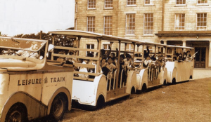 Vintage photo of a tractor puling carriages outside a hall