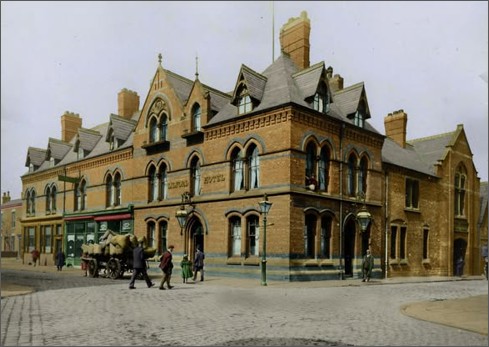 Large hotel set on the corner of two streets with people and old fashioned carts outside