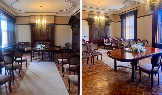 Elegant wood‑panelled ceremony room with chandeliers, arranged chairs, and floral displays on polished tables.