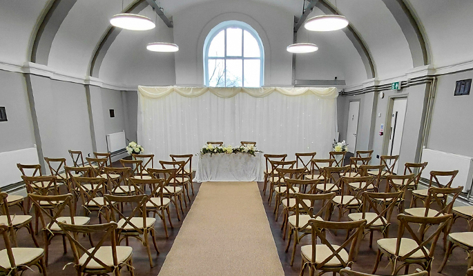 Wedding ceremony setup with rows of wooden chairs, aisle runner, and a white-draped table at the front.